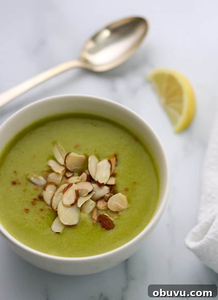 A bowl of zucchini soup topped with almonds with a lemon wedge and spoon