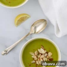 A bowl of zucchini soup topped with sliced almonds and a spoon and lemon wedge