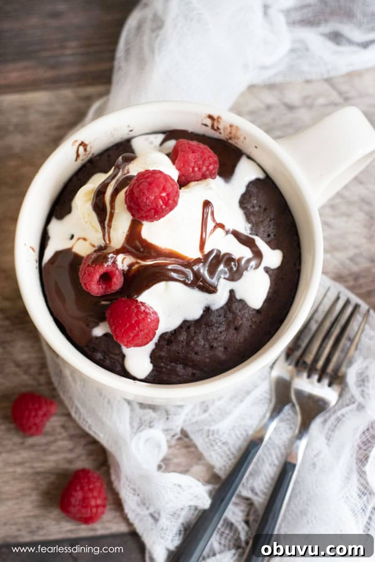 The top view of a chocolate mug cake in the mug topped with ice cream and raspberries.