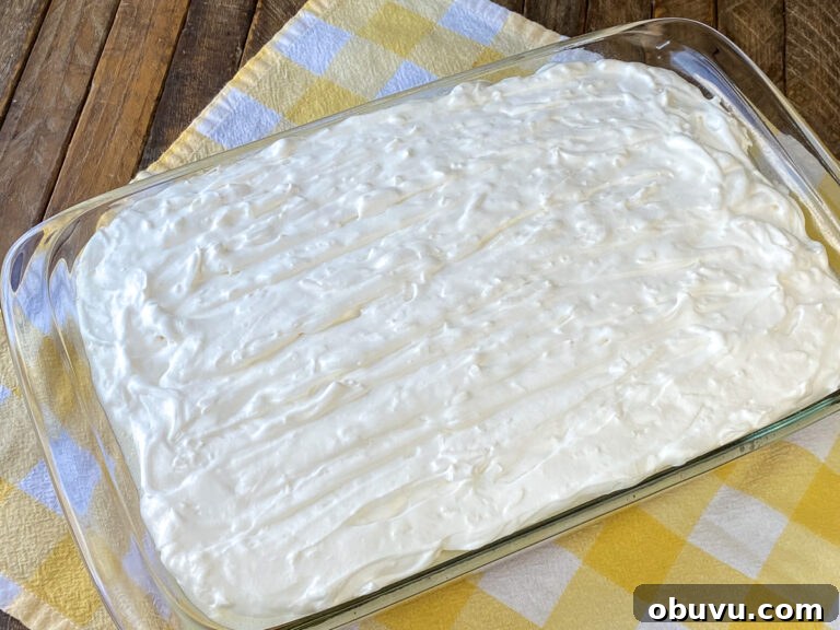 Thick layer of sour cream coconut frosting on a 9 x 13 cake on a yellow plaid napkin