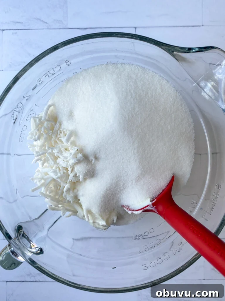 Sour cream, defrosted shredded coconut and sugar in a mixing bowl on a white counter top