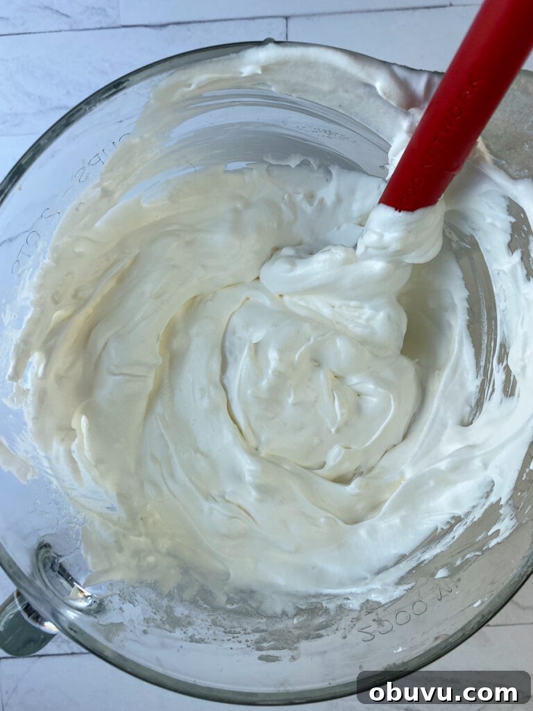 Cool whip being stirred into sour cream coconut cake frosting