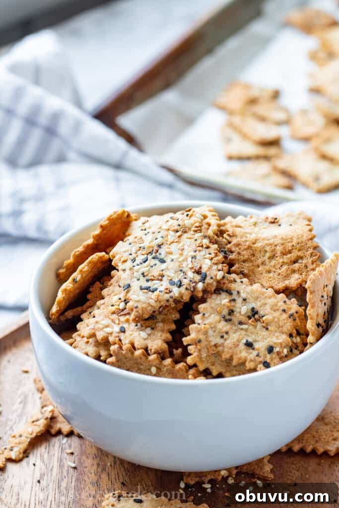 Baked sourdough crackers in white bowl on wood board.