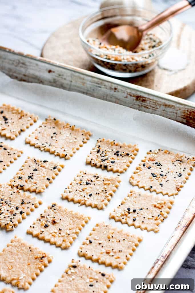 Raw sourdough crackers on baking sheet with bowl of spices in background.