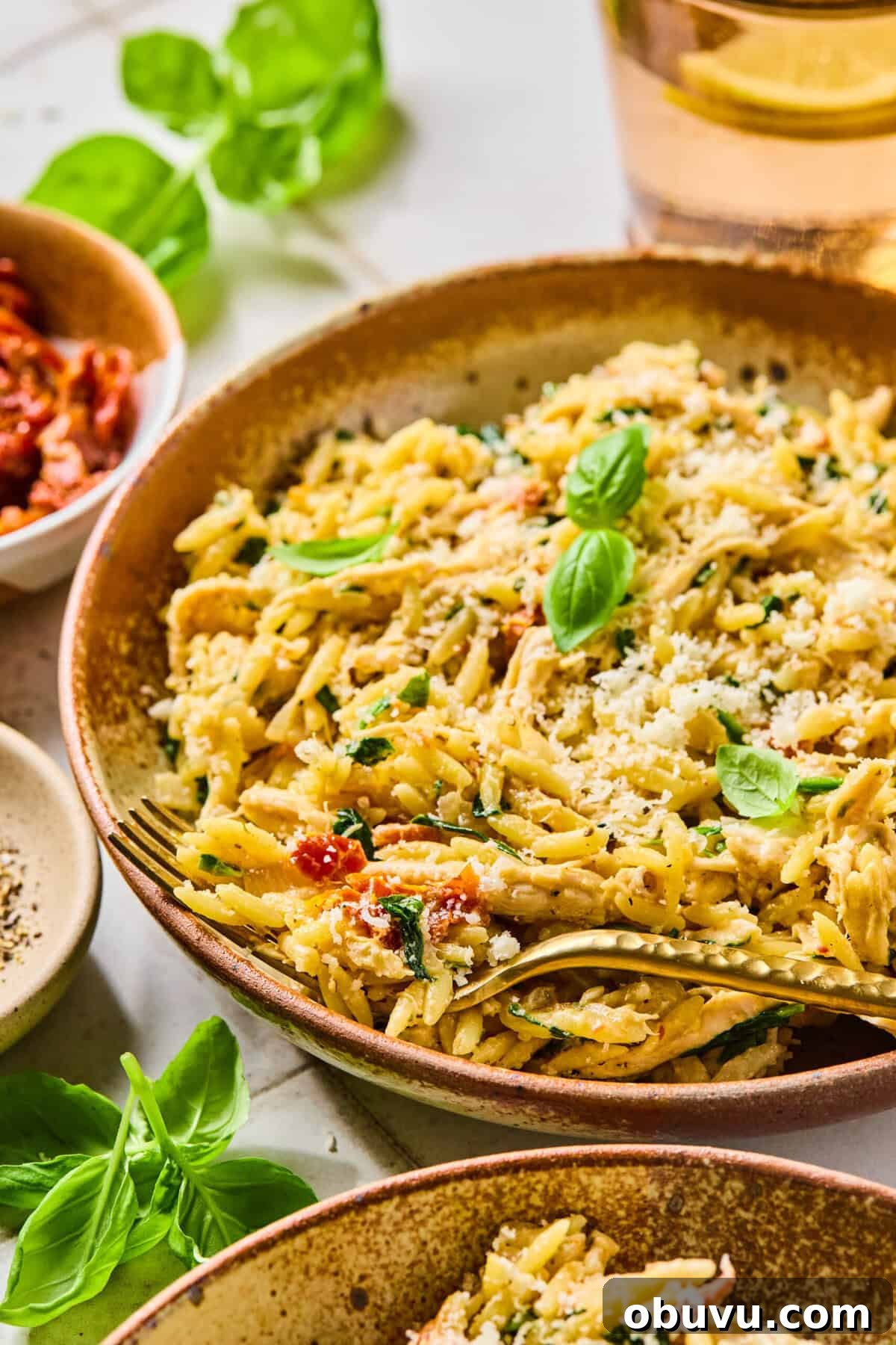 Gluten-Free Marry Me Chicken with Creamy Orzo 2 Marry me chicken orzo in a bowl with a fork lying in it. It’s garnished with fresh basil leaves.