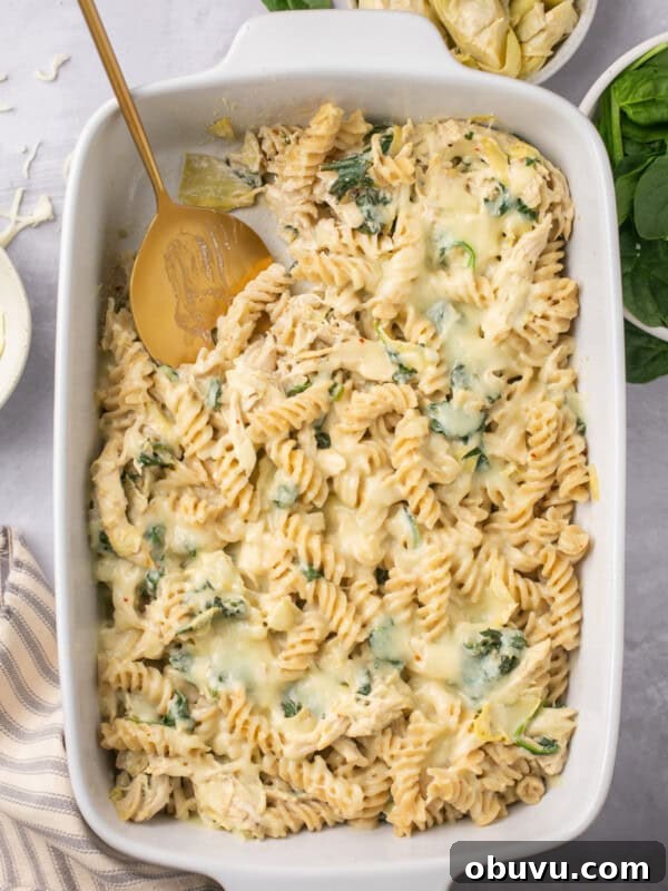 Gluten-Free Marry Me Chicken with Creamy Orzo 13 spinach artichoke chicken pasta bake in a casserole dish with a serving spoon taking a scoop out