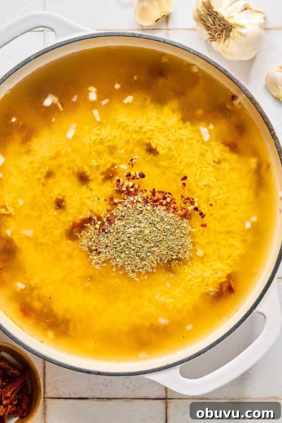 Gluten-Free Marry Me Chicken with Creamy Orzo 5 Gluten-free orzo simmering in chicken broth with Italian seasoning and red pepper in a skillet.