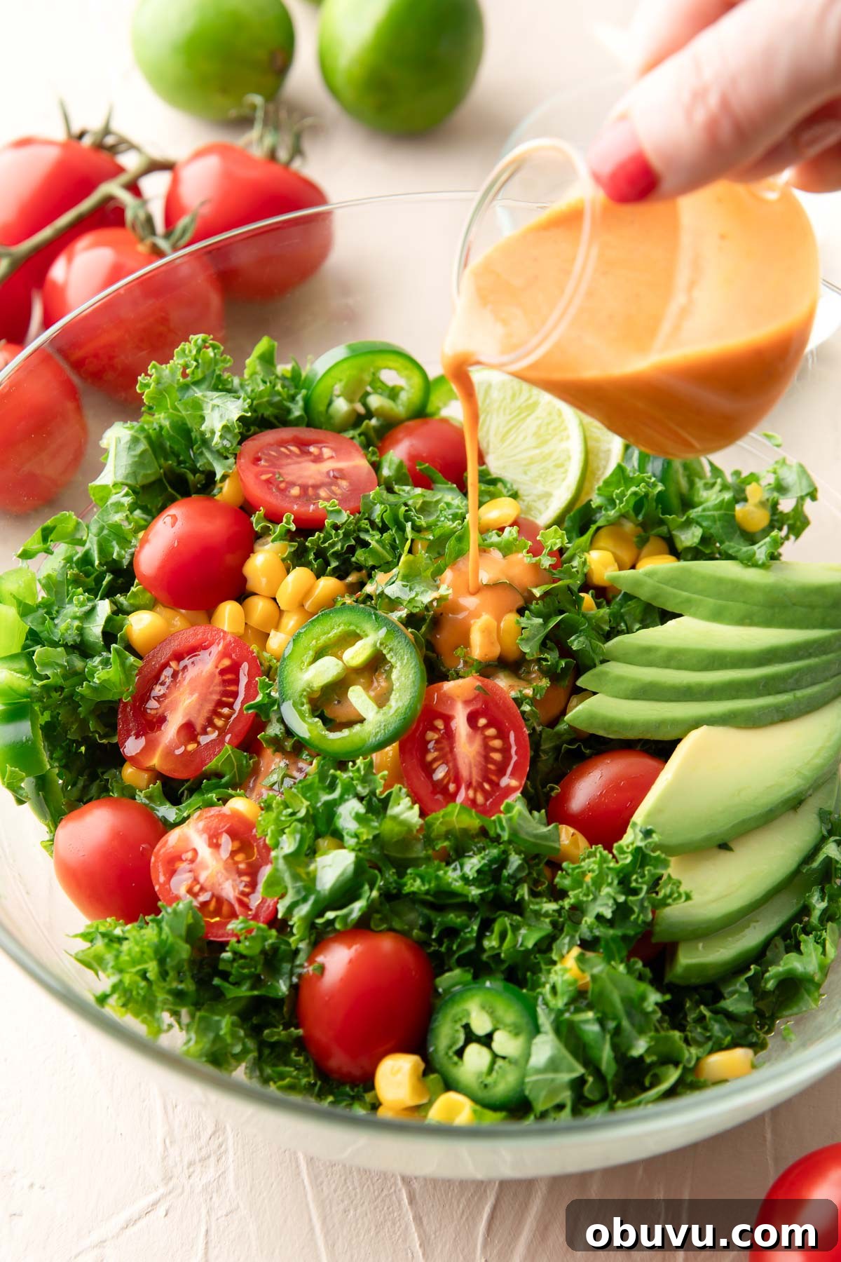 Chipotle Kale Salad Recipe with Smoky Lime Dressing 2 honey chipotle dressing being poured over kale salad with tomatoes, avocado, corn, bell peppers, and jalapeno