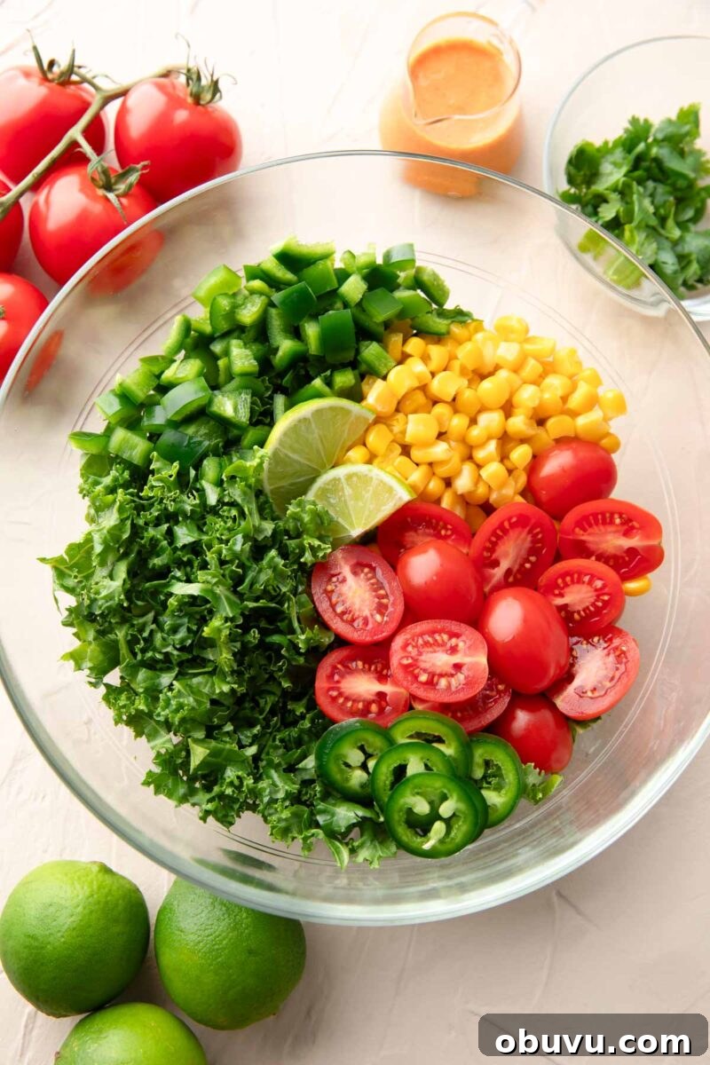 Chipotle Kale Salad Recipe with Smoky Lime Dressing 5 glass mixing bowl with kale salad ingredients added in rows: tomatoes, peppers, corn, lime