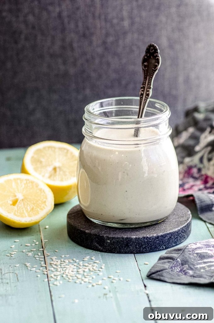 A jar with spicy tahini dressing  next to a lemon cut in half on a green wood surface
