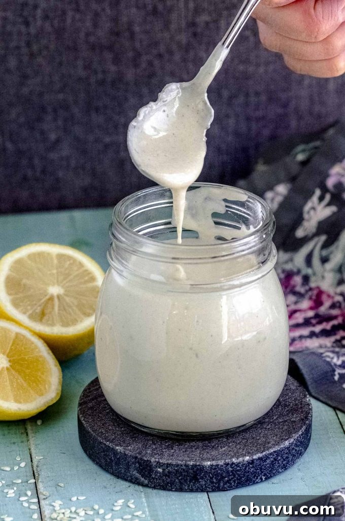 Scooping some spicy tahini dressing from a jar next to a lemon cut in half