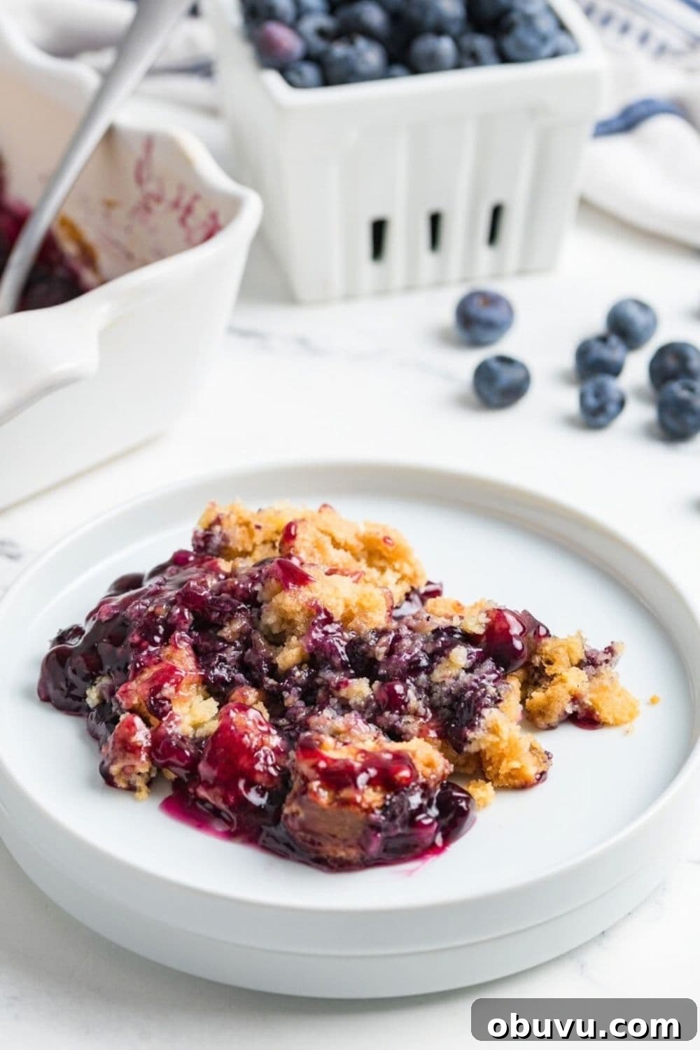 Blueberry Cobbler Dump Cake Made with Muffin Mix 5 a serving of warm blueberry dump cake on a white plate.