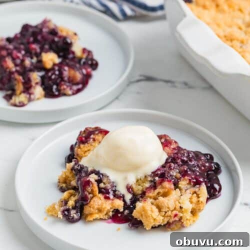 Blueberry Cobbler Dump Cake Made with Muffin Mix 10 Blueberry cobbler dump cake served on white plates, with the baking dish of remaining cobbler in the background.