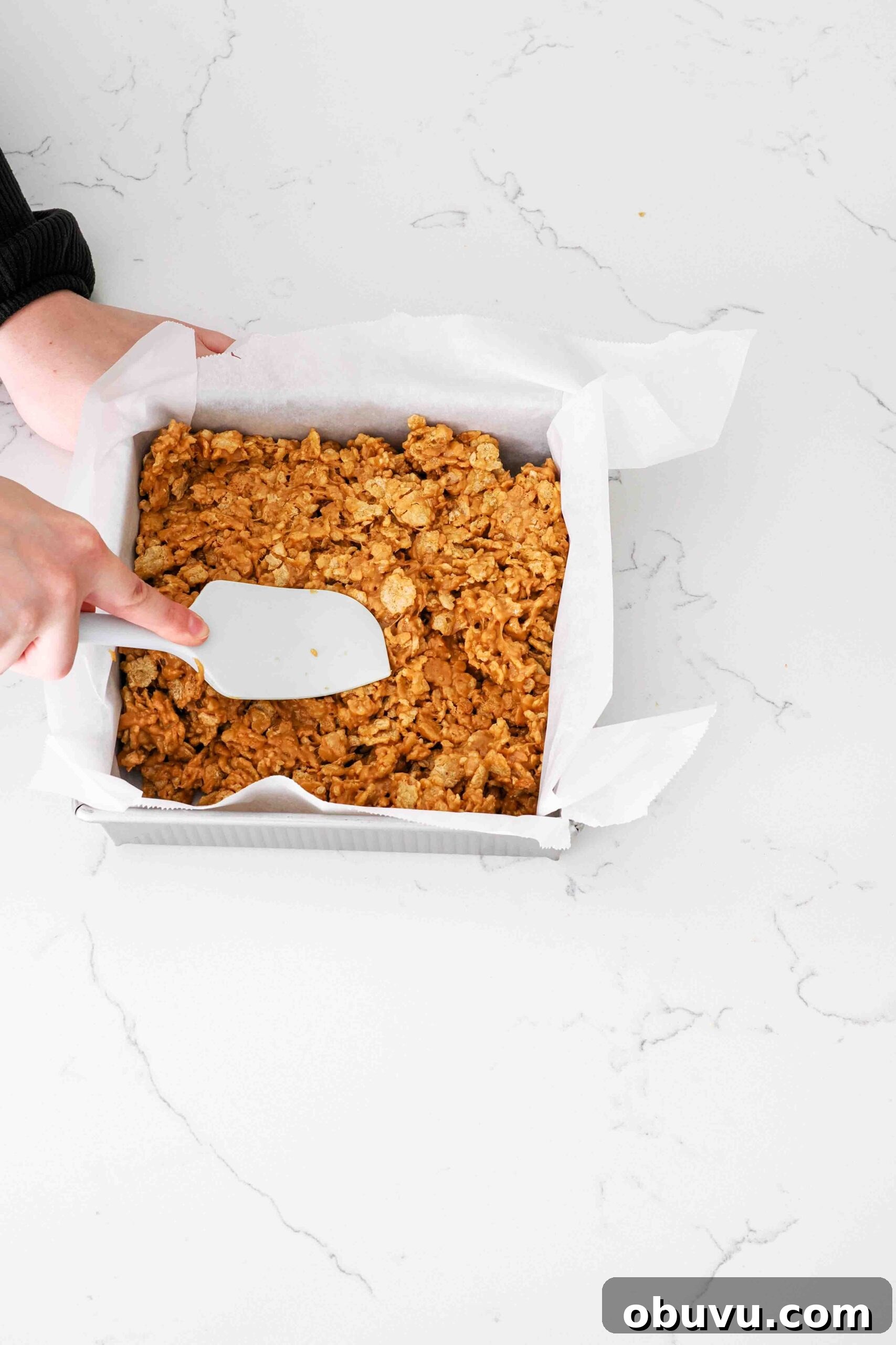 Aunt Deb’s Special K Bars Recipe — Crispy Cereal Treats 6 A hand uses a spatula to press Special K bars into a square pan.