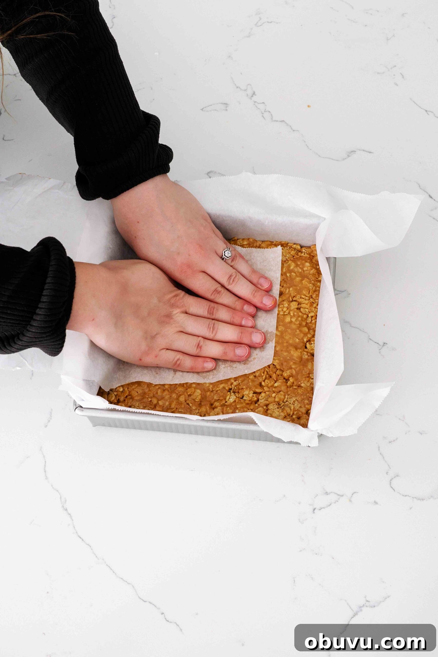 Aunt Deb’s Special K Bars Recipe — Crispy Cereal Treats 7 Two hands press Special K bars into a square pan with a piece of parchment paper.