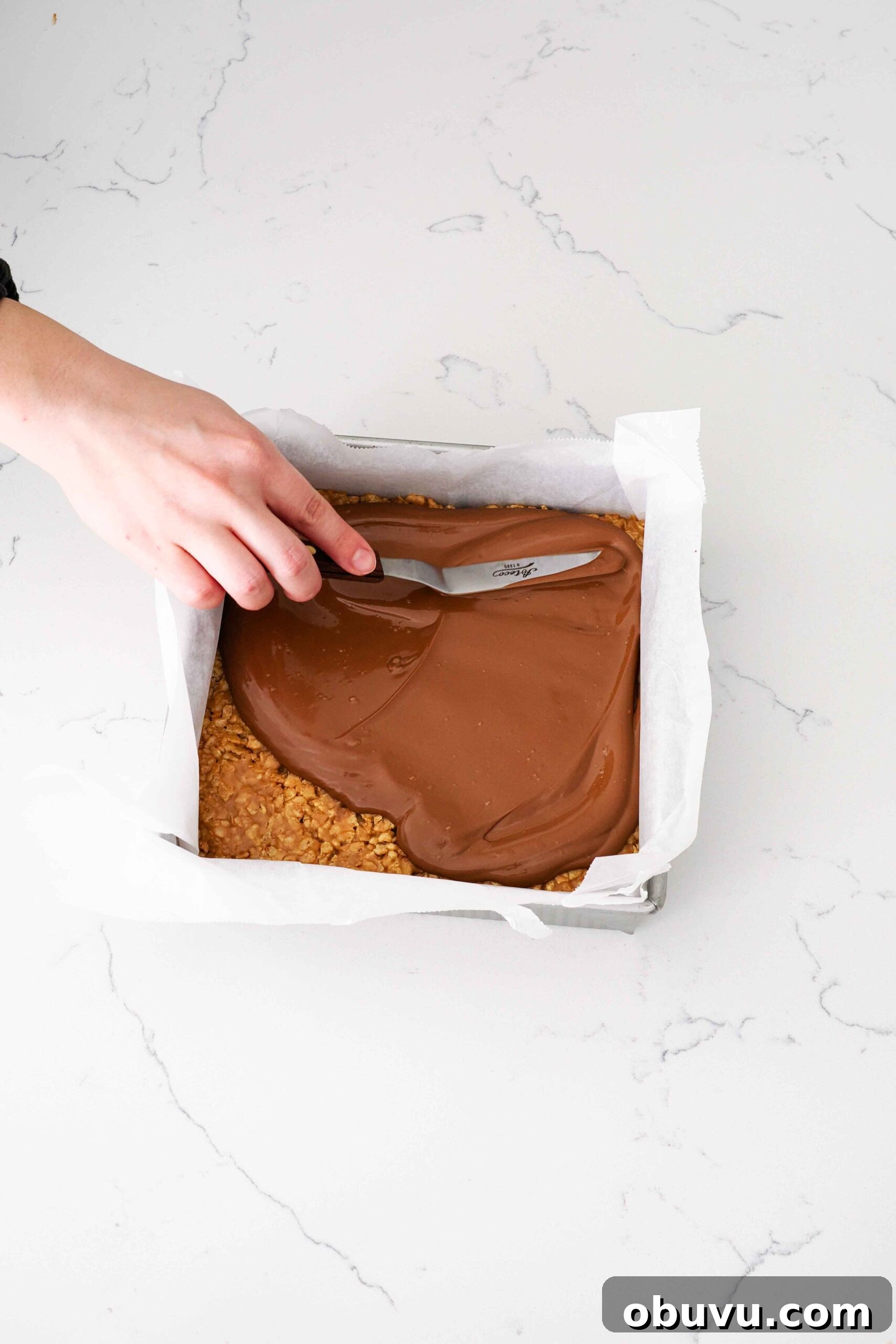 Aunt Deb’s Special K Bars Recipe — Crispy Cereal Treats 8 An offset spatula spreads chocolate topping over Special K bars.