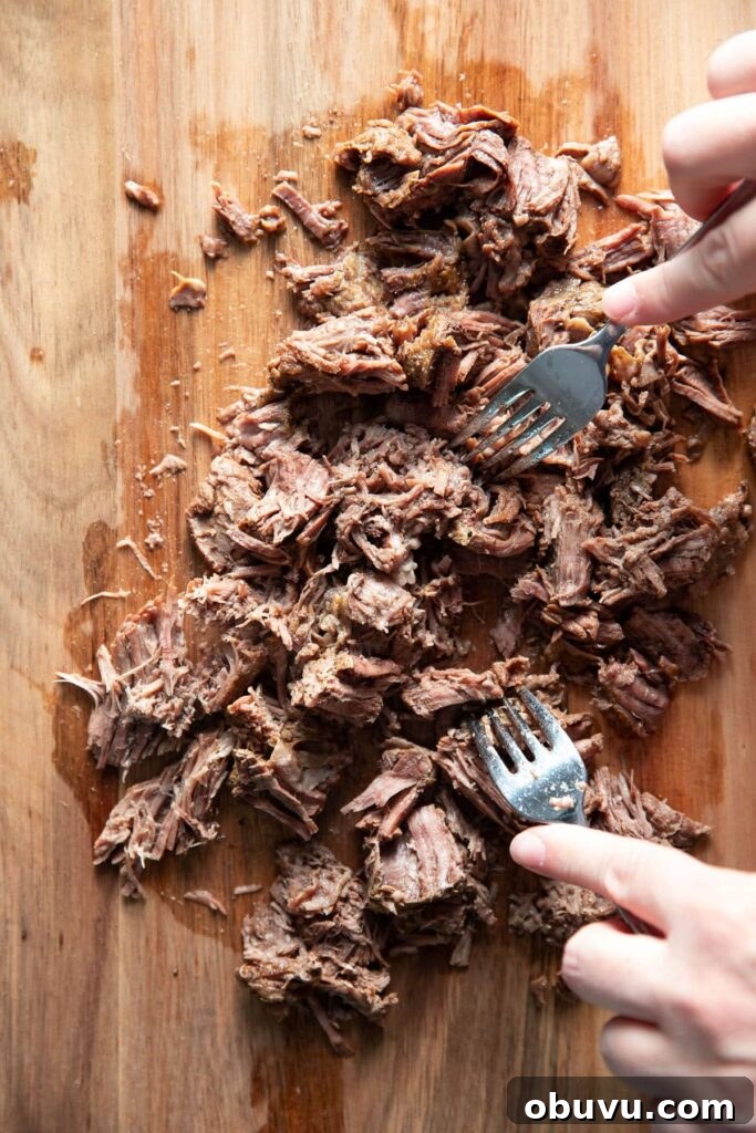 shredding a pot roast with forks on a cutting board