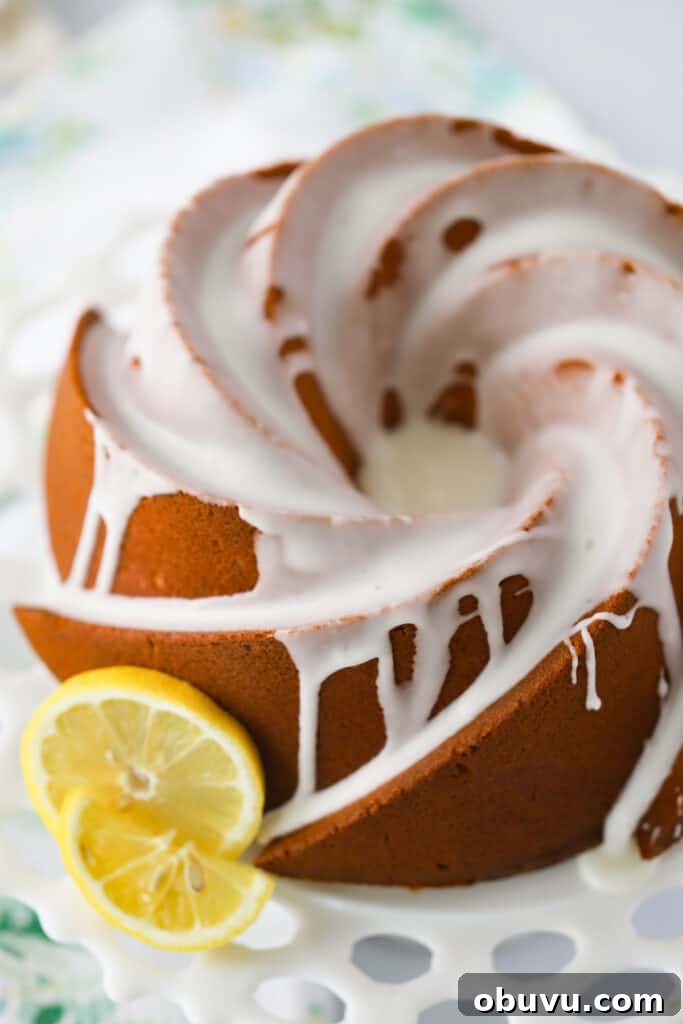 Classic Lemon Pound Cake Recipe — Moist & Zesty Slice 2 A glazed Lemon Pound Cake with cream cheese on a cake stand topped with glaze.