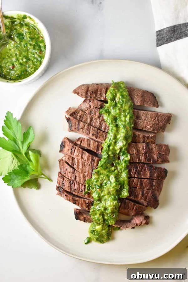 Sliced flank steak on a plate with chimichurri sauce on top and parsley