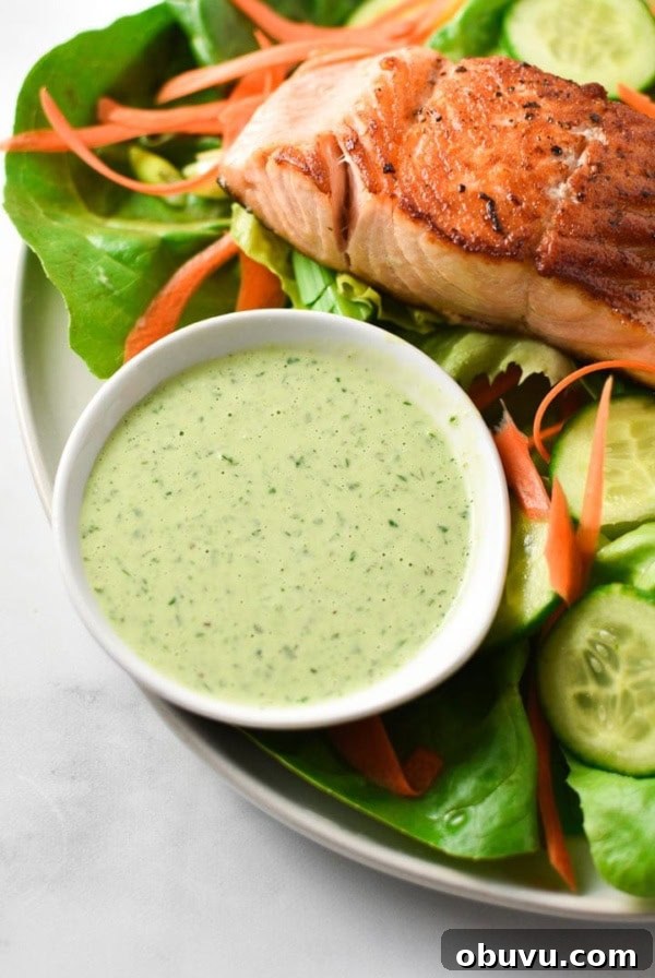 A bowl of creamy basil dressing next to seared salmon on a green salad