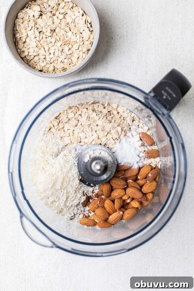 A food processor bowl with oatmeal, coconut, almonds and sea salt.
