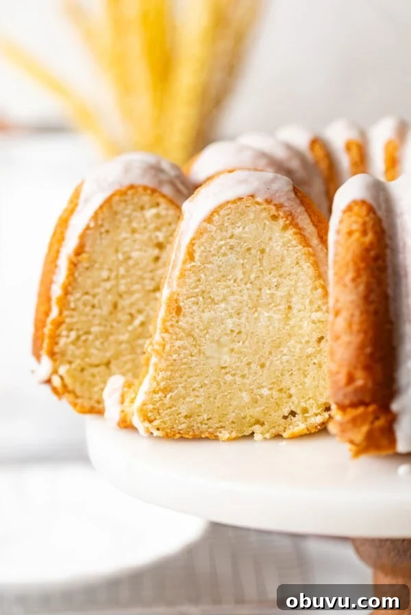 sliced sour cream pound cake on a cake stand topped with vanilla glaze.
