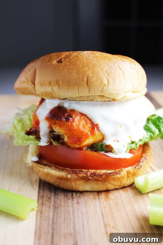 Spicy Buffalo Chicken Breast Burger Recipe 6 A Buffalo chicken burger with cheese, ranch, tomato and lettuce on a wooden cutting board