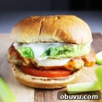 Spicy Buffalo Chicken Breast Burger Recipe 8 A Buffalo chicken burger with cheese, ranch, tomato and lettuce on a wooden cutting board