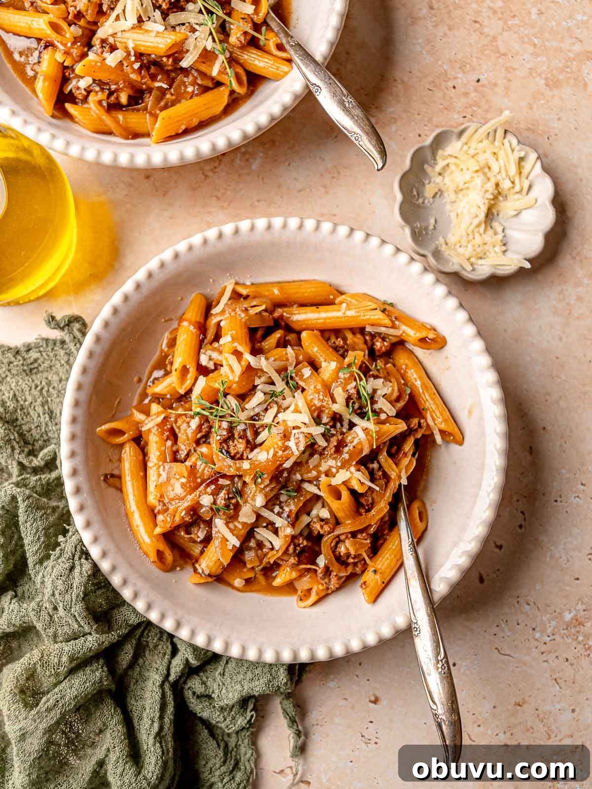 Creamy French Onion Soup Pasta Made in One Pot 2 Creamy French onion soup pasta in white bowls next to a small bowl of Parmesan cheese and a jar of olive oil.
