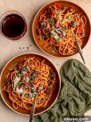 Two bowls of pasta next to a glass of wine.