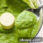 How to make avocado herb green sauce: A spoon lifting out a small amount of sauce from the food processor to show the creamy texture.