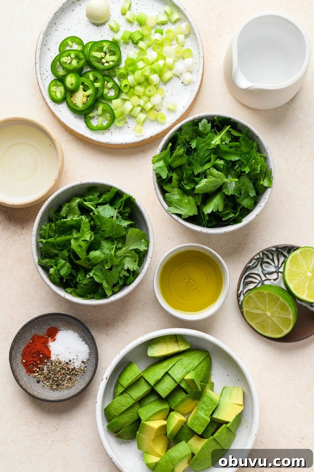 Ingredients for Avocado Herb Green Sauce in various ceramics, on a light cream colored background.