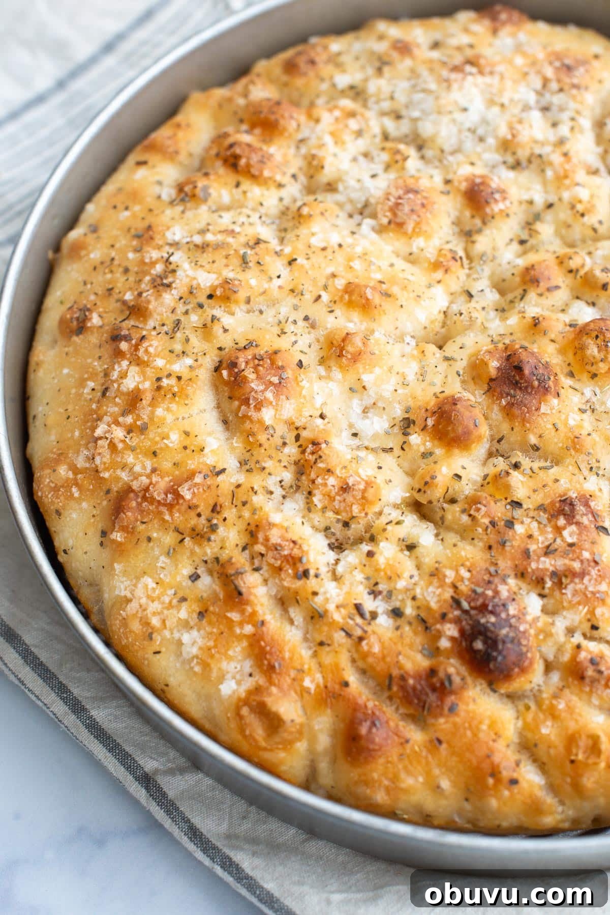 Sourdough Focaccia: Crispy, Airy Italian-Style Loaf Recipe 4 Sourdough Focaccia bread in a round pan on a kitchen towel.
