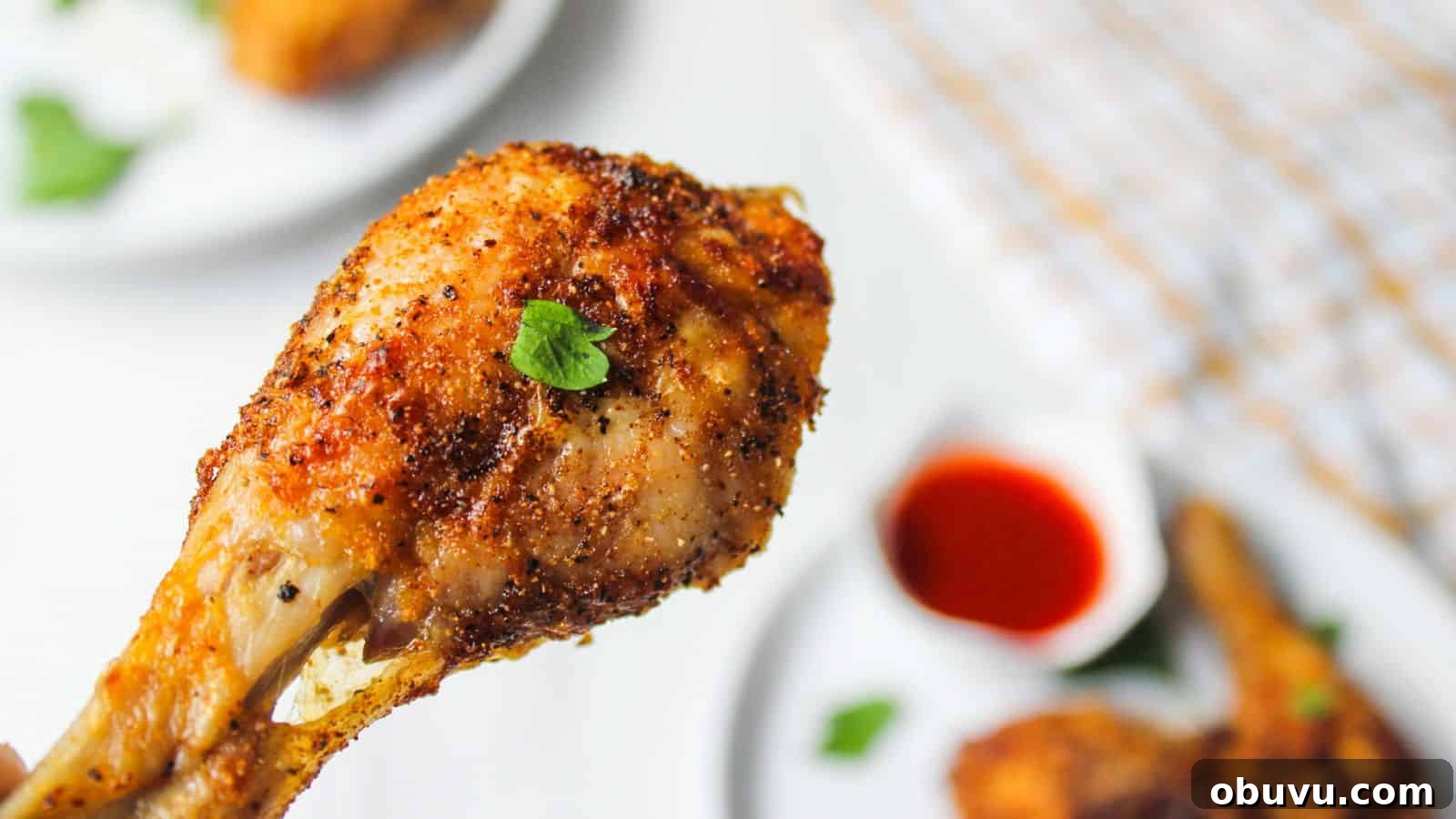 29 Delicious Low-Carb Meals That Aren’t Just Salad 11 Close-up of a crispy air fried chicken drumstick on a white plate garnished with parsley, with hot sauce in the background.