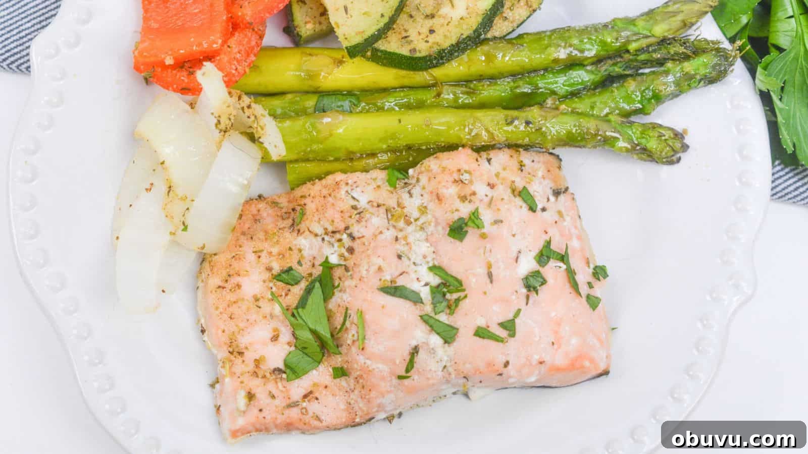 29 Delicious Low-Carb Meals That Aren’t Just Salad 10 Baked salmon fillet with asparagus, zucchini, and bell peppers on a white plate, garnished with herbs.