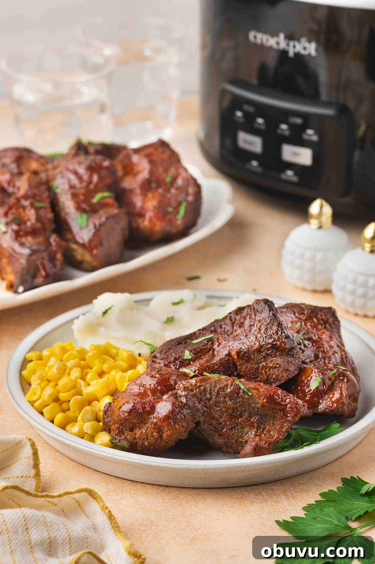 Tender Country-Style Ribs in the Slow Cooker: Simple Recipe 2 A plate of slow cooker country style ribs with corn and mashed potatoes with a slow cooker in the background and more ribs.