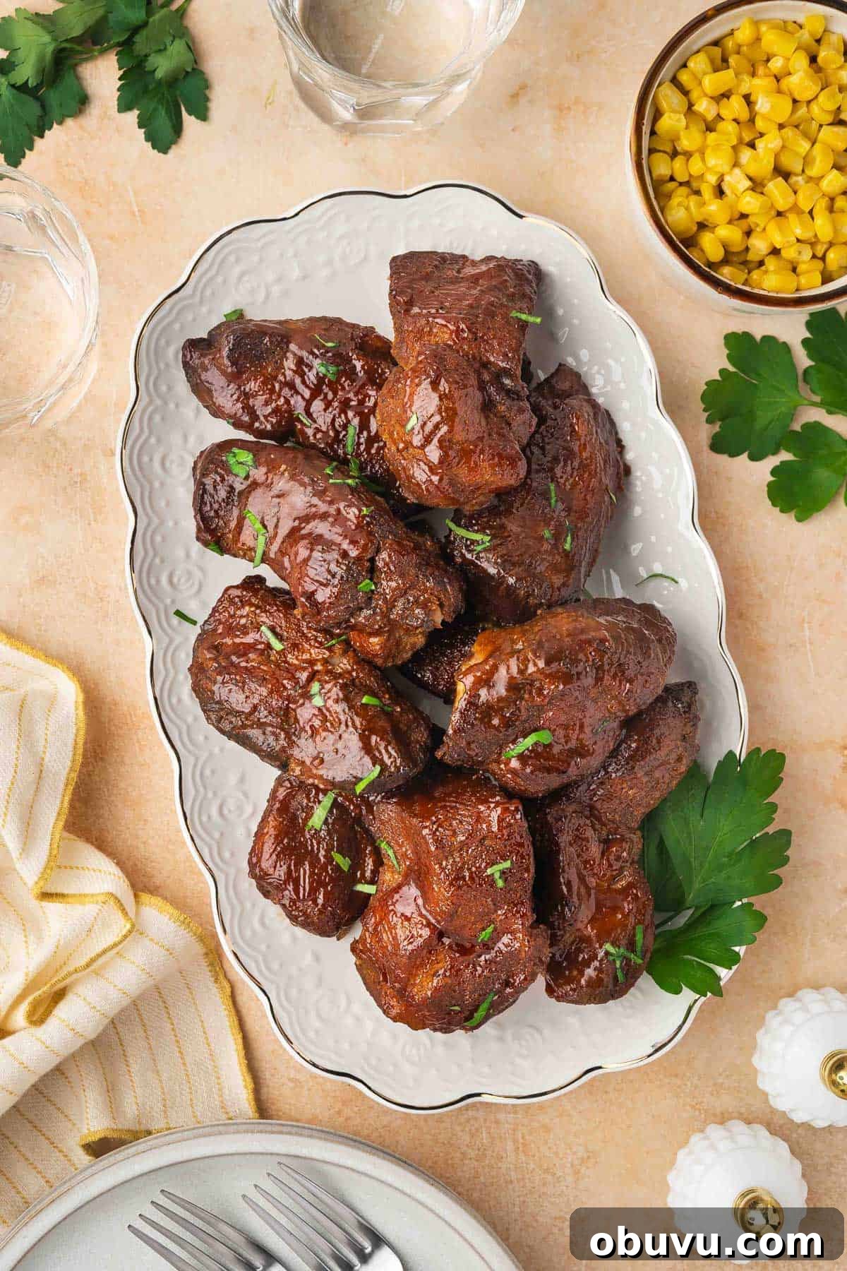 Tender Country-Style Ribs in the Slow Cooker: Simple Recipe 9 An overhead view of a platter of slow cooker country style ribs with some parsley garnish. A small bowl of corn on the side.
