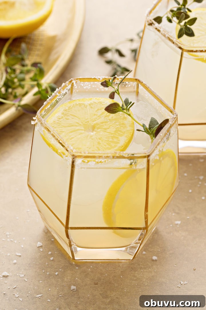 photo of a lemon margarita on a gold background, garnished with lemon slices and fresh thyme