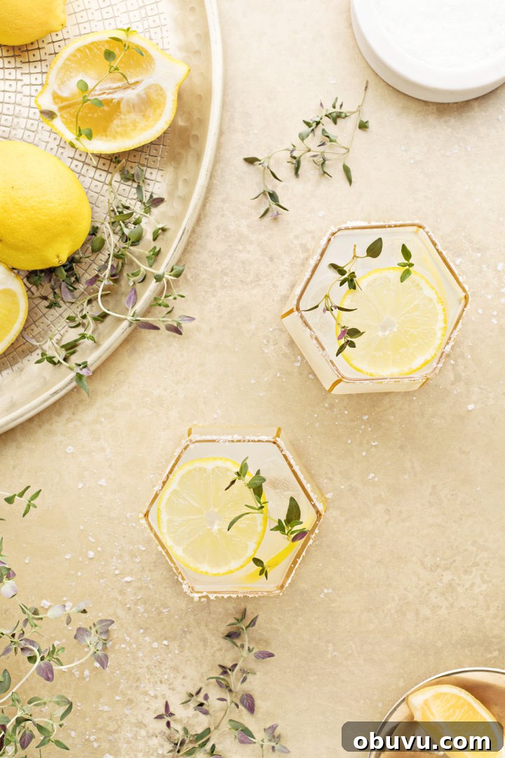 overhead photo of two lemon margaritas on a gold background with fresh thyme and lemon