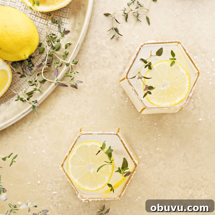 overhead photo of two lemon margaritas on a gold background with fresh thyme and lemon