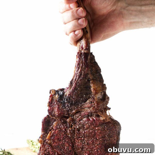 Maple Bourbon Smash Cocktail Recipe — Warm Autumn Whiskey Smash 12 seared tomahawk steak being held vertically from the bone, resting on cutting board