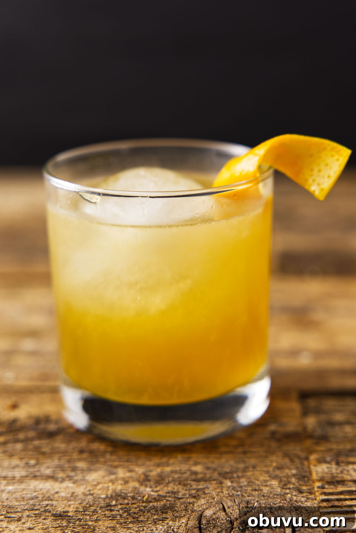 Maple Bourbon Smash Cocktail Recipe — Warm Autumn Whiskey Smash 13 Glass filled with orange bourbon cocktail with orange peel twist and globe ice.