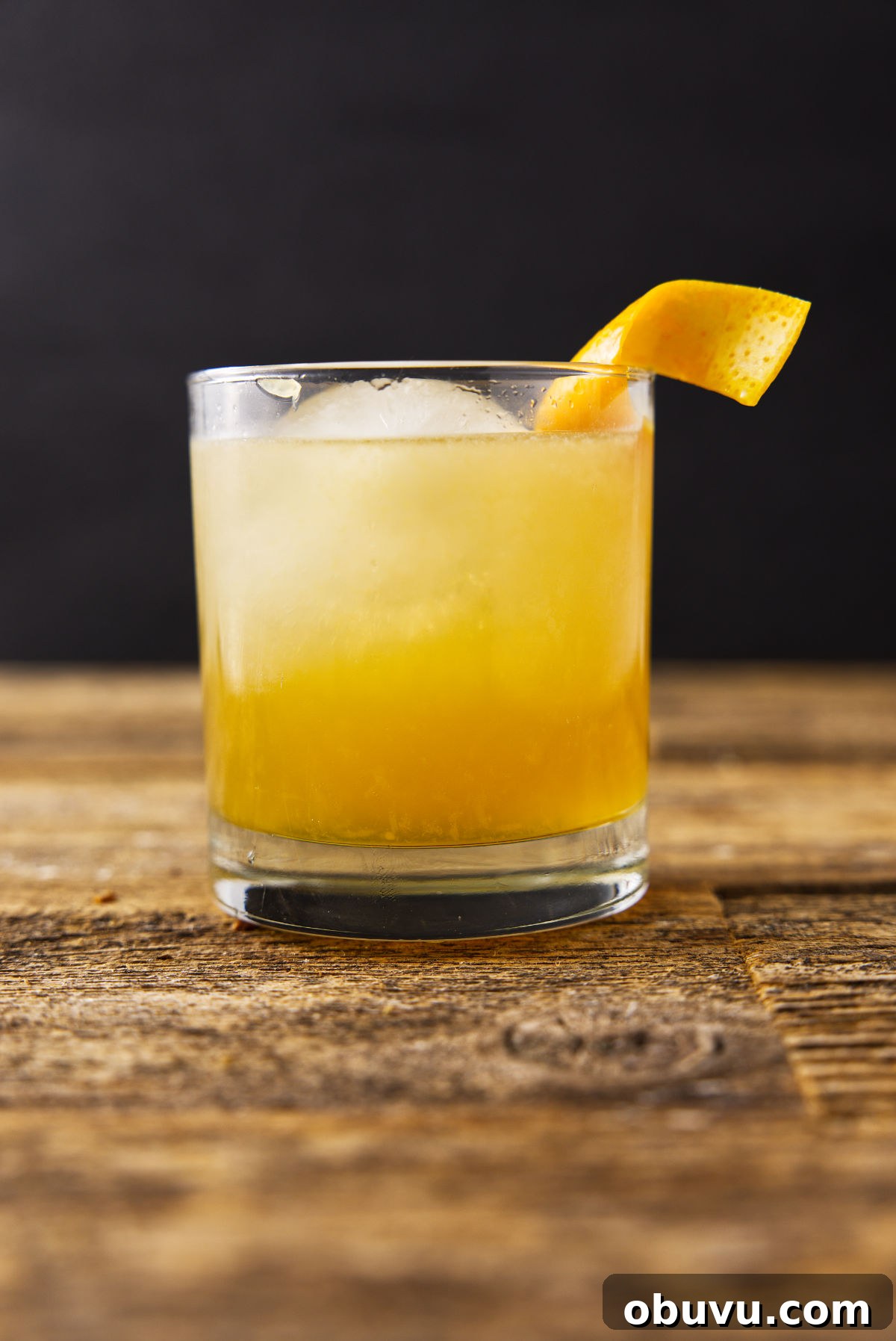 Maple Bourbon Smash Cocktail Recipe — Warm Autumn Whiskey Smash 3 Glass filled with maple bourbon smash with an orange peel twist hanging on the rim of the glass.