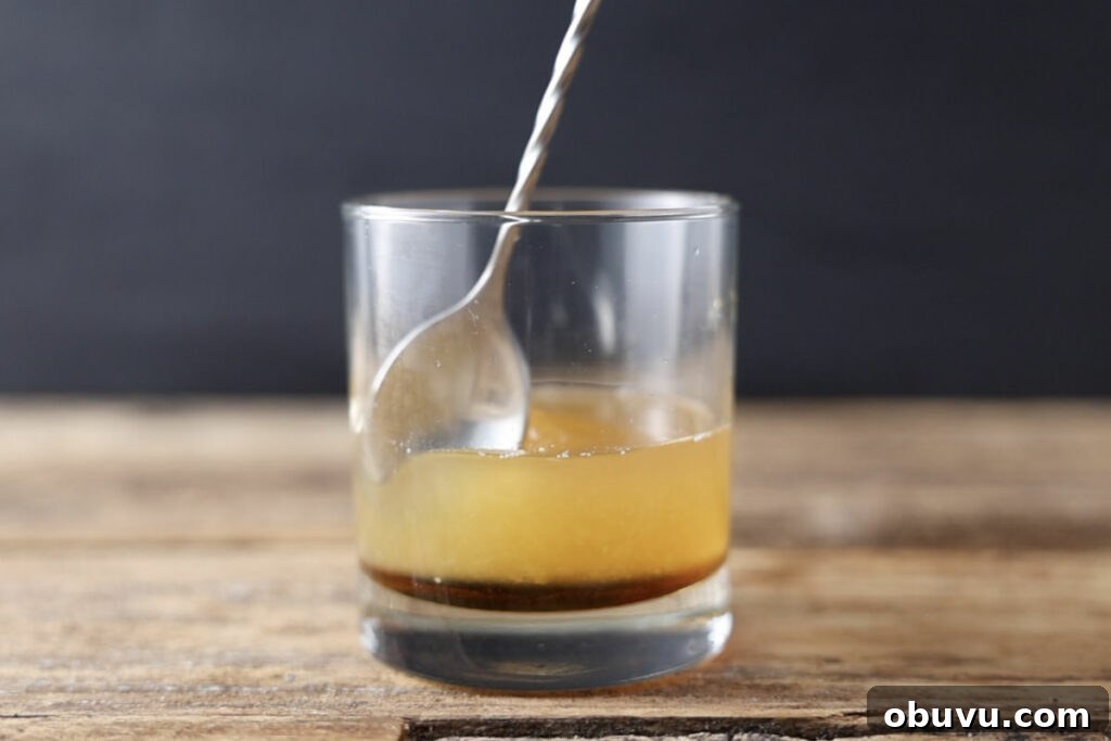 Maple Bourbon Smash Cocktail Recipe — Warm Autumn Whiskey Smash 6 Stirring maple bourbon smash in glass.