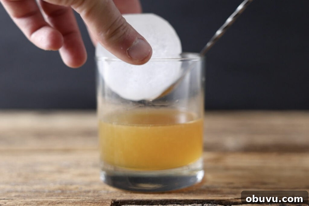 Maple Bourbon Smash Cocktail Recipe — Warm Autumn Whiskey Smash 7 Adding sphere ice to cocktail glass.
