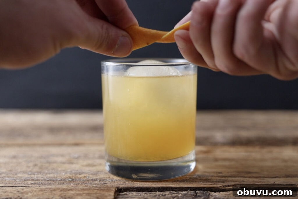 Maple Bourbon Smash Cocktail Recipe — Warm Autumn Whiskey Smash 9 Expressing orange peel over cocktail.
