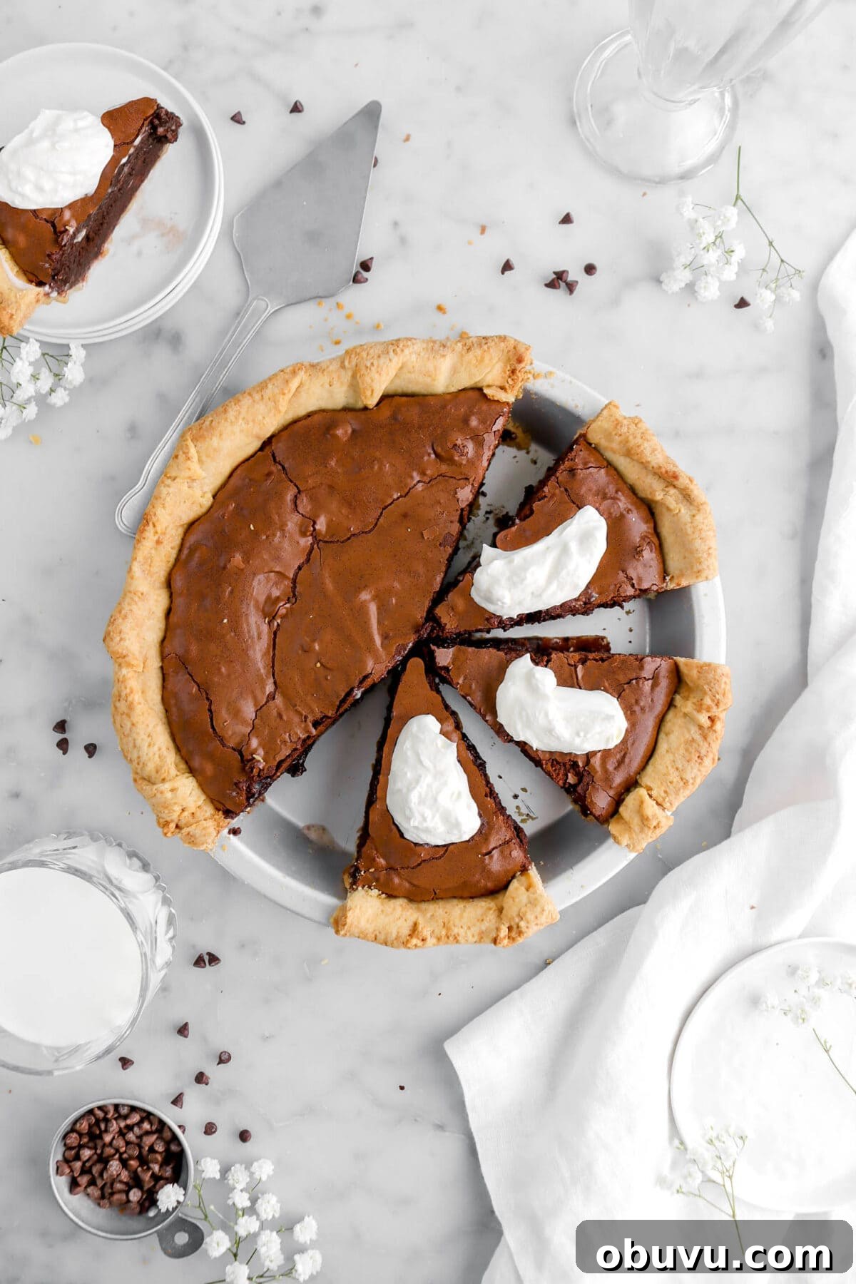 Fudgy Chocolate Chip Brownie Pie Recipe for Ooey-Gooey Dessert 3 brownie pie with three in pie plate and whipped cream decorating each piece, another slice of pie on stack of white plates beside.