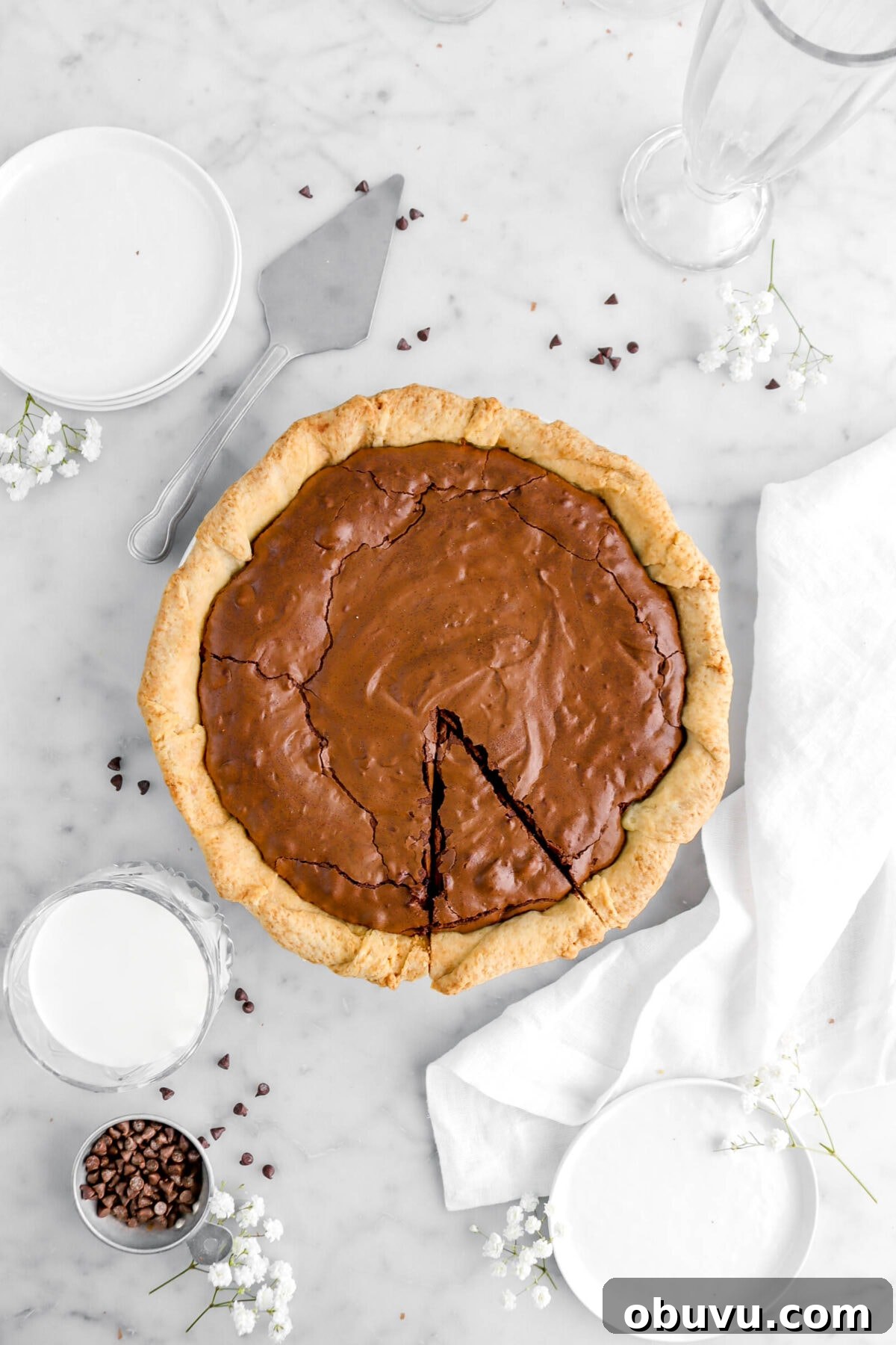 Fudgy Chocolate Chip Brownie Pie Recipe for Ooey-Gooey Dessert 12 brownie pie with slice cut into it with white flowers and chocolate chips around.