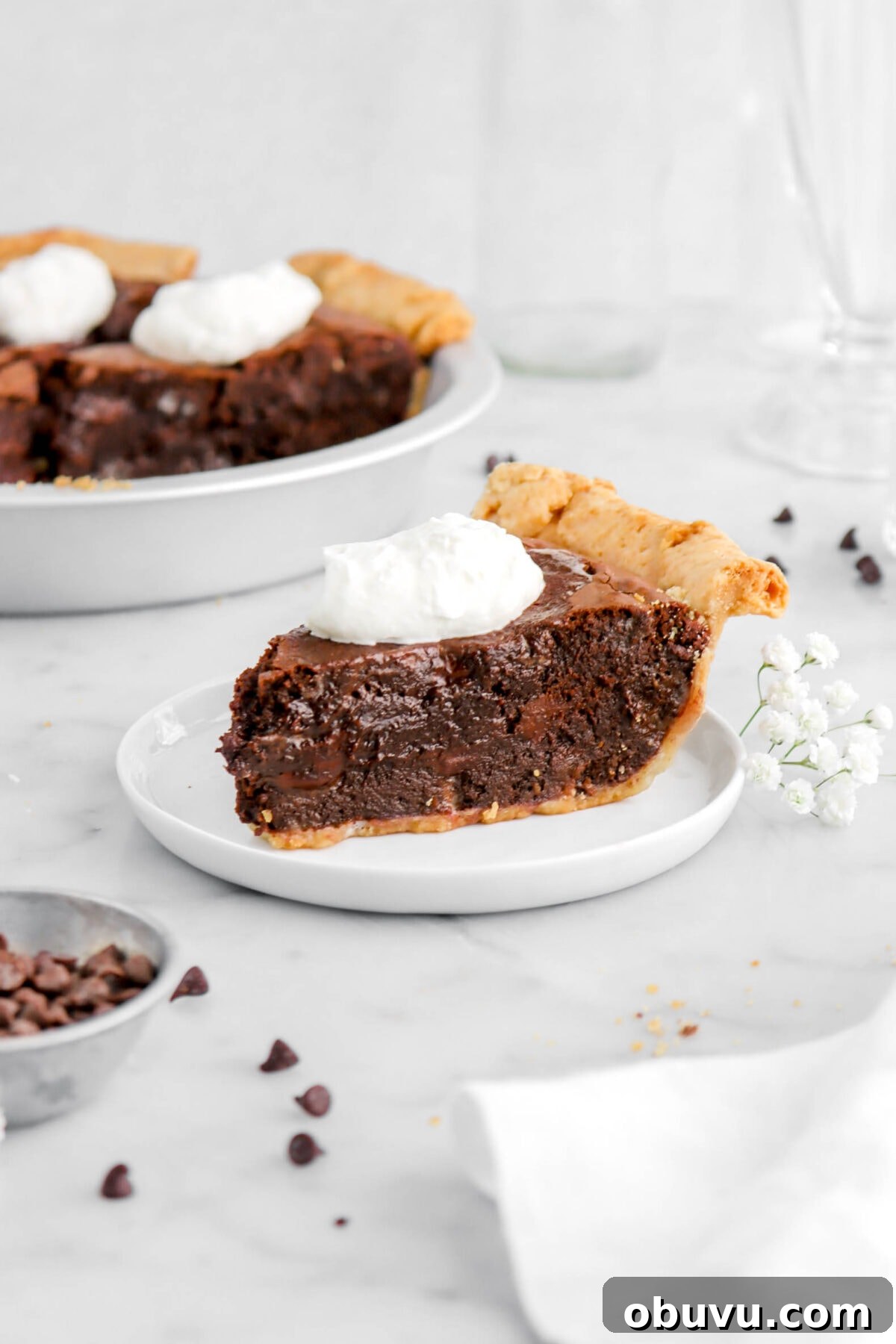 Fudgy Chocolate Chip Brownie Pie Recipe for Ooey-Gooey Dessert 5 slice of brownie pie on white plate with full pie behind in metal pie plate on marble surface.