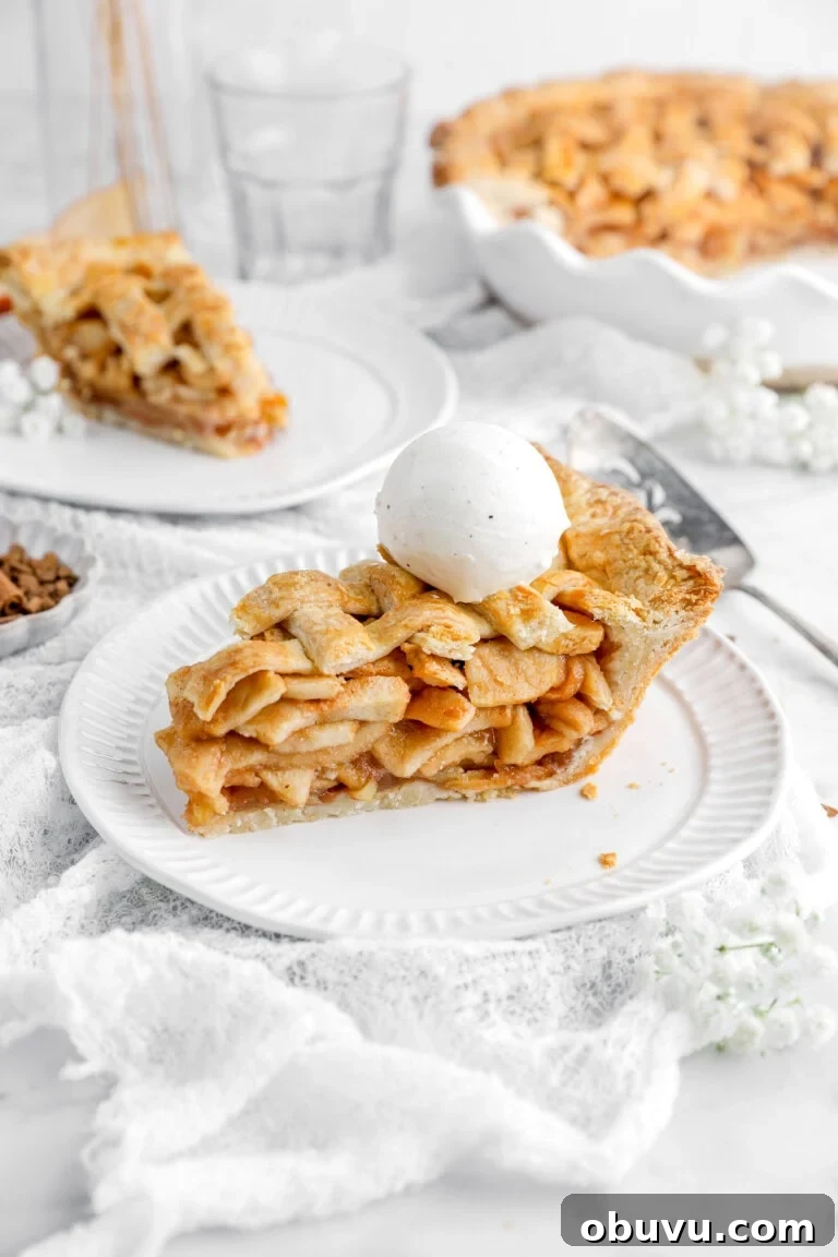 slice of apple pie with ice cream scoop on top and another slice of pie behind.